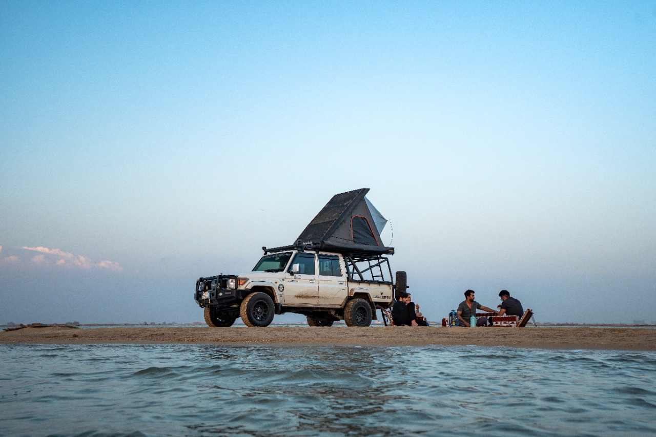 A 4x4 with a rooftop tent parked at the water's edge