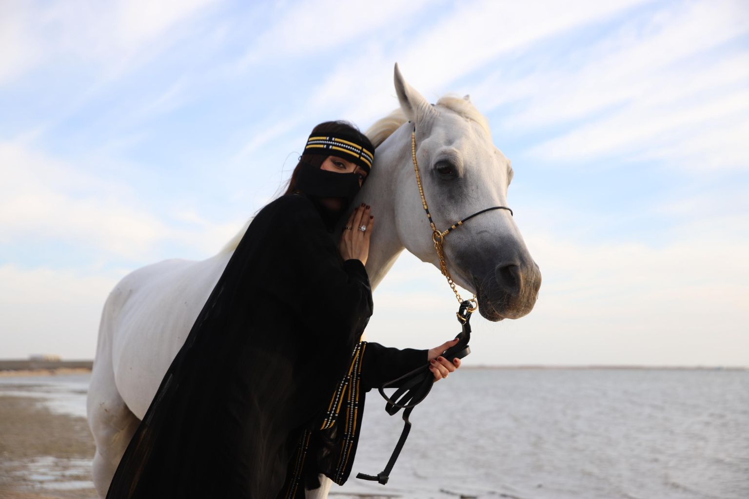 A rider leading her white horse along the Jeddah shore